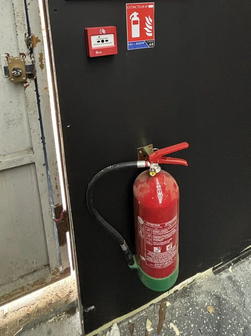 Extincteur installé sur un support mural, avec déclencheur manuel et signalétique à proximité.