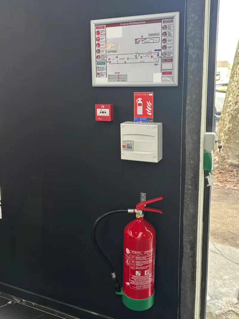 Installation de sécurité incendie avec plan d’intervention anonymisé, extincteur, déclencheur manuel et signalétique.